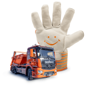 Ein weisser Arbeitshandschuh mit orangefarbenen Streifen und einem aufgemalten lachenden Gesicht steht aufrecht. Davor ist ein oranger Lastwagen mit blauer Plane geparkt.
