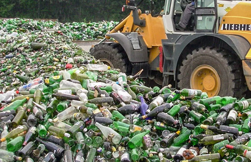 Alte Glasflaschen auf dem Recyclinghof, dazwischen ein Radlader